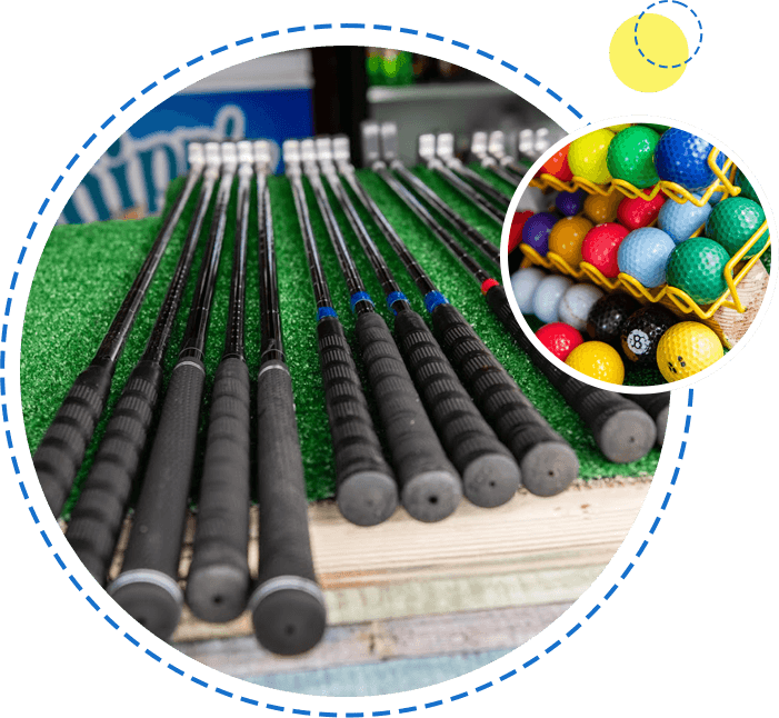Golf clubs in a row on artificial grass and a rack of colorful golf balls in the background.