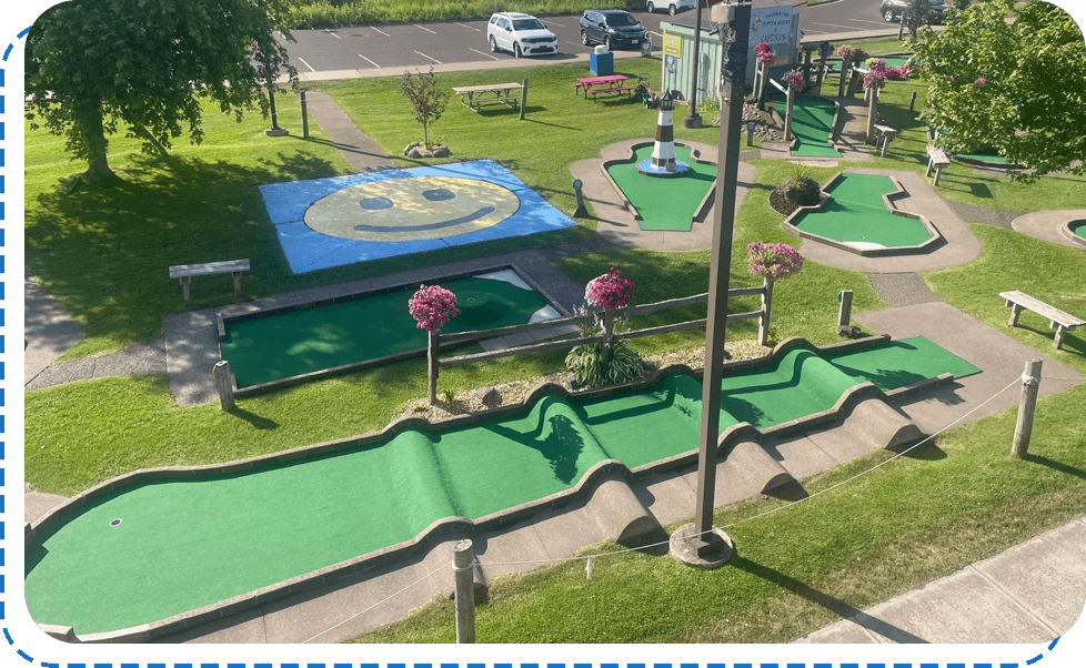 Aerial view of a vibrant outdoor mini-golf course with green carpets, surrounded by flowering plants and benches.